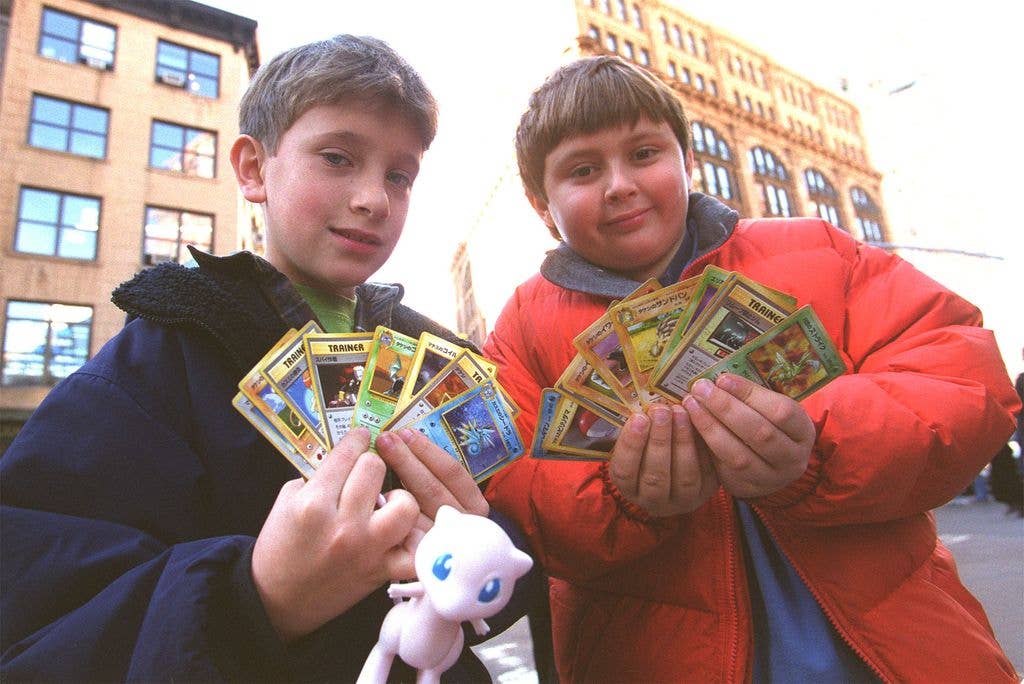 Two children hold up fans of Pokemon cards, one holds a pink Pokemon doll.