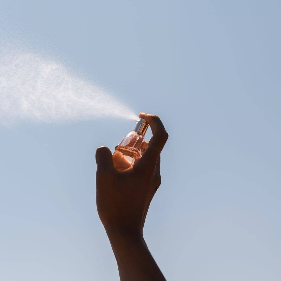 A hand spritzing perfume into the sky