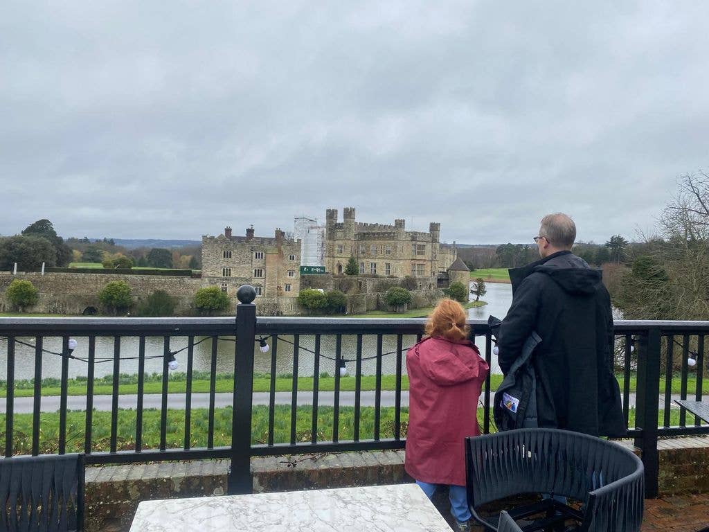 Man and girl standing on a balcony looking out at a moat and castle