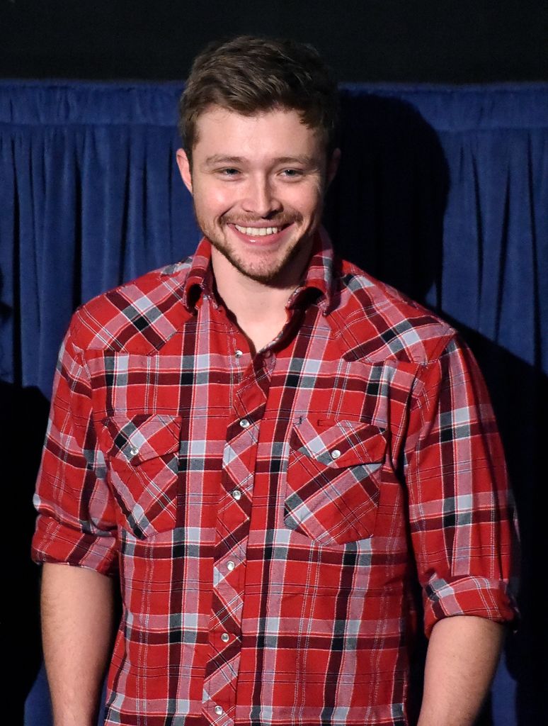 Sterling Knight stands wearing a red flannel shirt and puts his hands in his pockets.