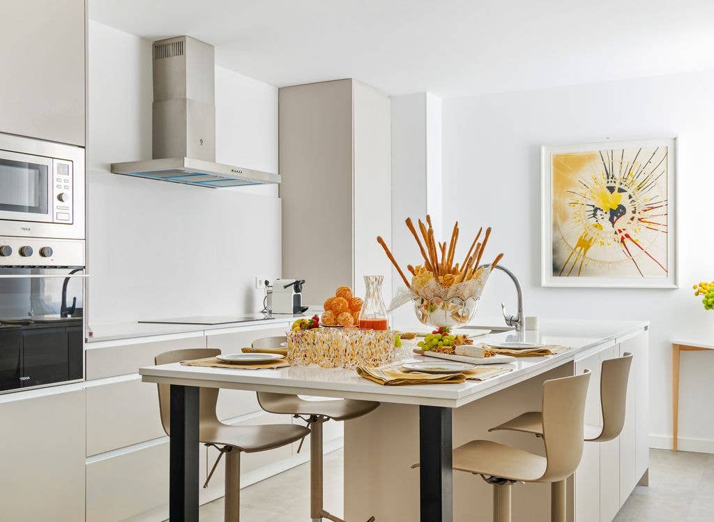 The kitchen features a breakfast table surrounded by four chairs, set against white walls with clean, modern lines and an art piece on the wall inside designer Silvia Tcherassi's Madrid home 