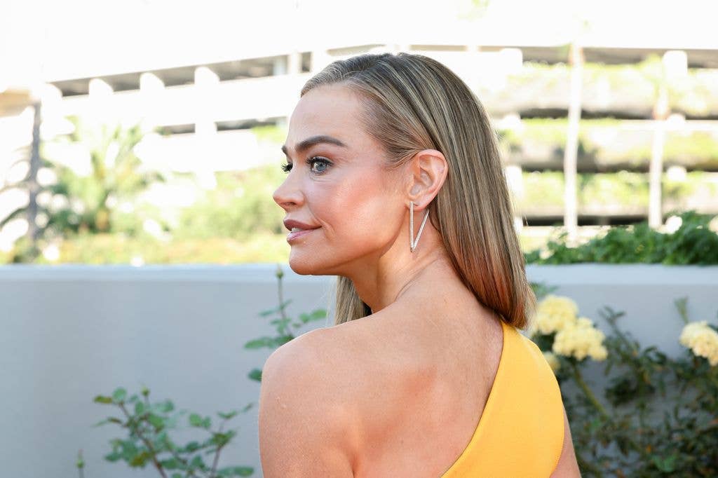 Denise Richards looking over her shoulder wearing a yellow one shoulder top