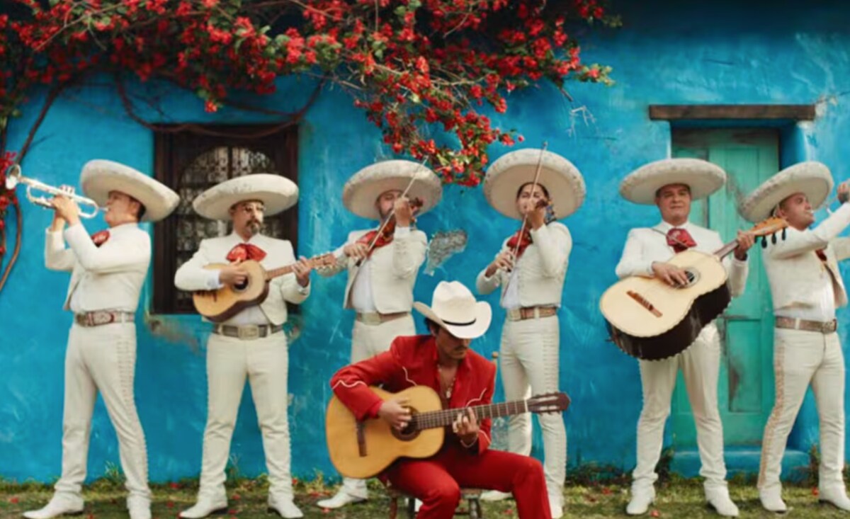 Mars sits against a bright blue wall, surrounded by a mariachi band dressed in white.