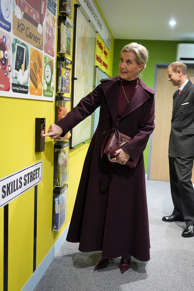 The Duchess of Edinburgh pointing at wall in burgundy dress and boots