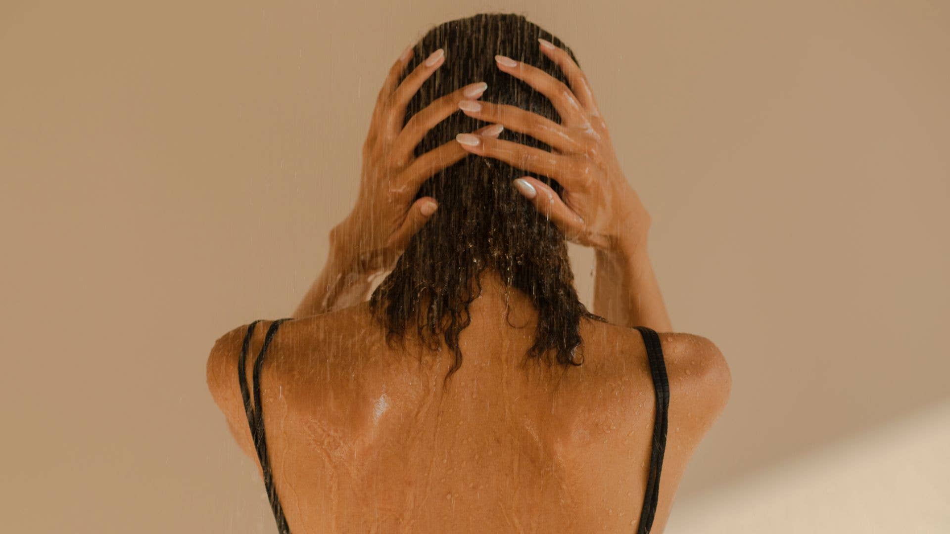 A woman with her back to the camera wearing a balck swimming costume in the shower
