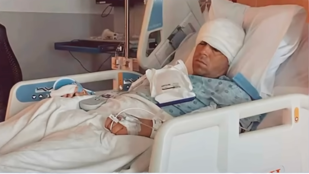 Gary in hospital bed with bandage around his head