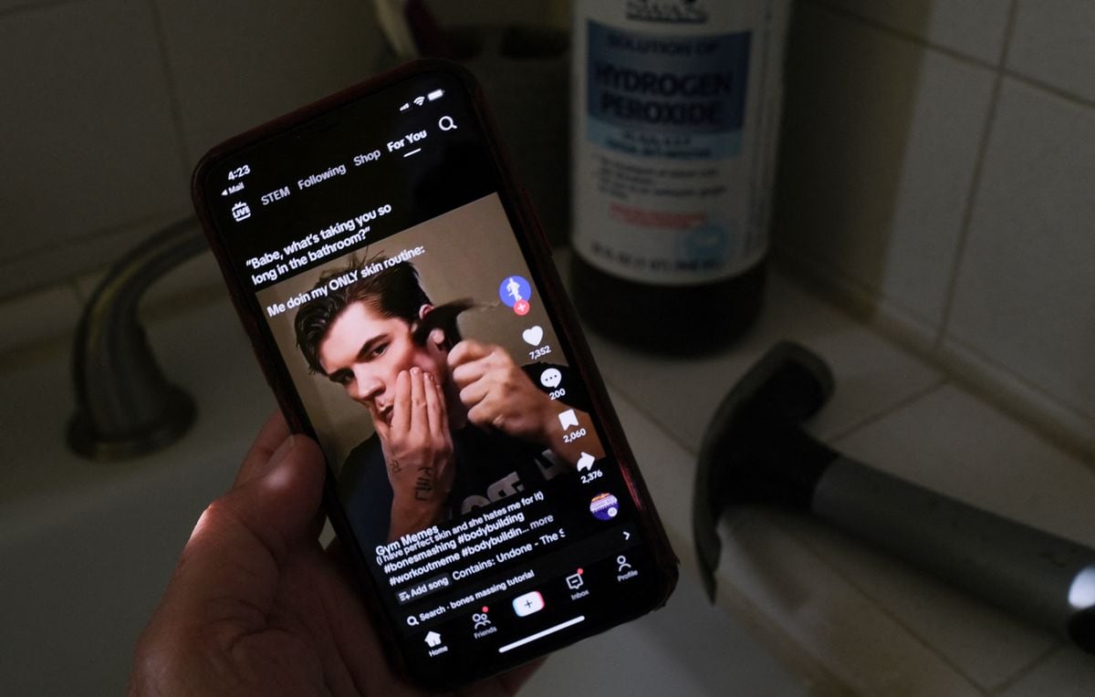 This illustration photo shows a video of male TikTok influencer hammering his cheekbone, playing on a smartphone in a bathroom next to a bottle of hydrogen peroxide and a hammer in Los Angeles, April 11, 2025. Hankering for a perfectly angular jaw, a male TikTok influencer hits his cheekbones with a hammer -- part of the popular online "looksmaxxing" trend that promotes unproven and often dangerous techniques to boost sexual appeal. Looksmaxxing influencers -- part of an online ecosystem dubbed the "manosphere" -- have surged in popularity across social media, capitalizing on the insecurities of young men eager to boost their physical attractiveness to women. (Photo by Chris DELMAS / AFP) (Photo by CHRIS DELMAS/AFP via Getty Images)
