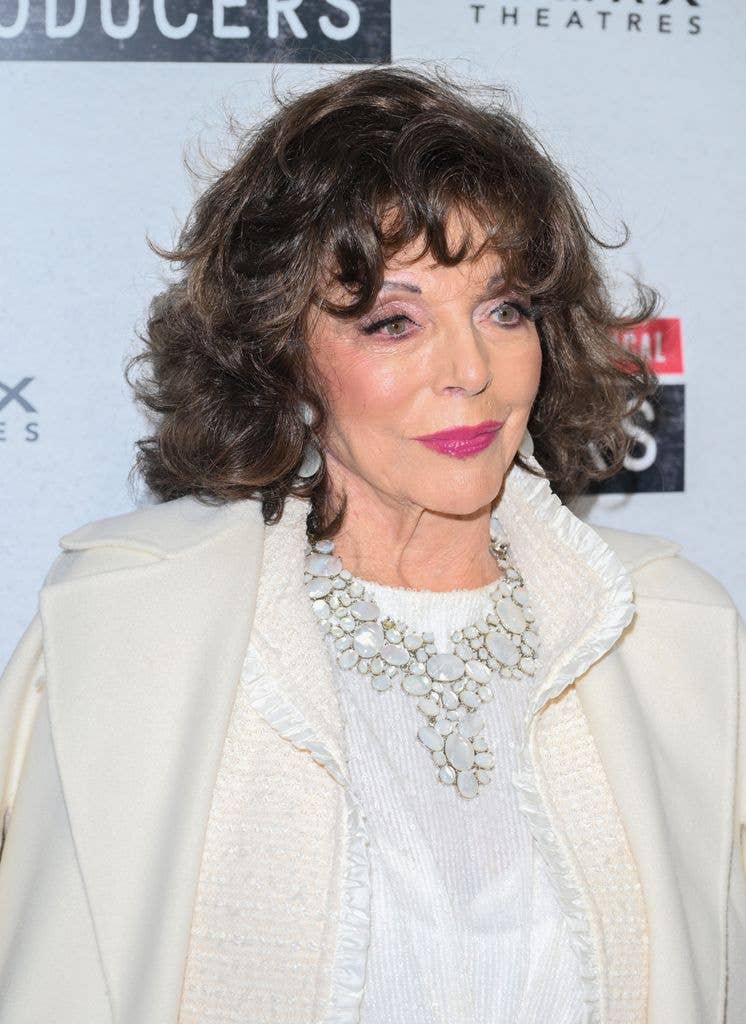 Dame Joan Collins looking to right in white coat