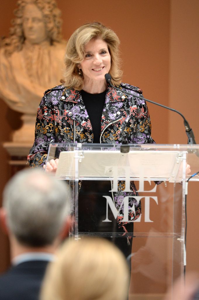 Caroline Kennedy stands behind a clear podium reading The Met.