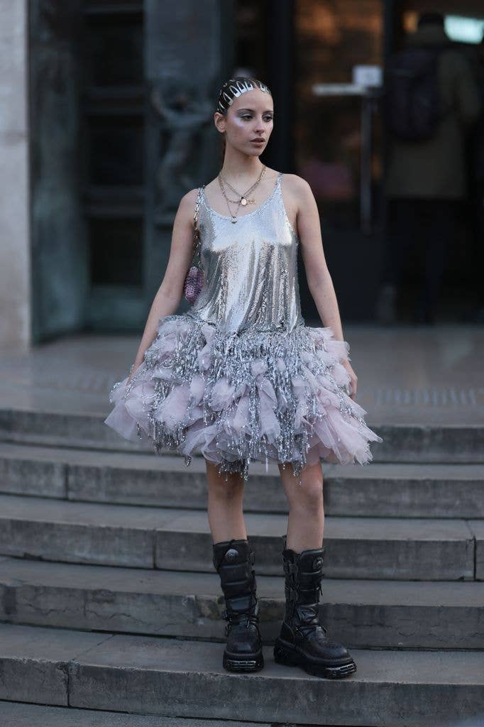 Marie Gaguech wears silver hair clips, a silver metallic tutu dress with glitter and pink details at the skirt, a pink glitter handbag and black boots, outside Paco Rabanne , during Paris Fashion Week on March 01, 2023 in Paris, France.