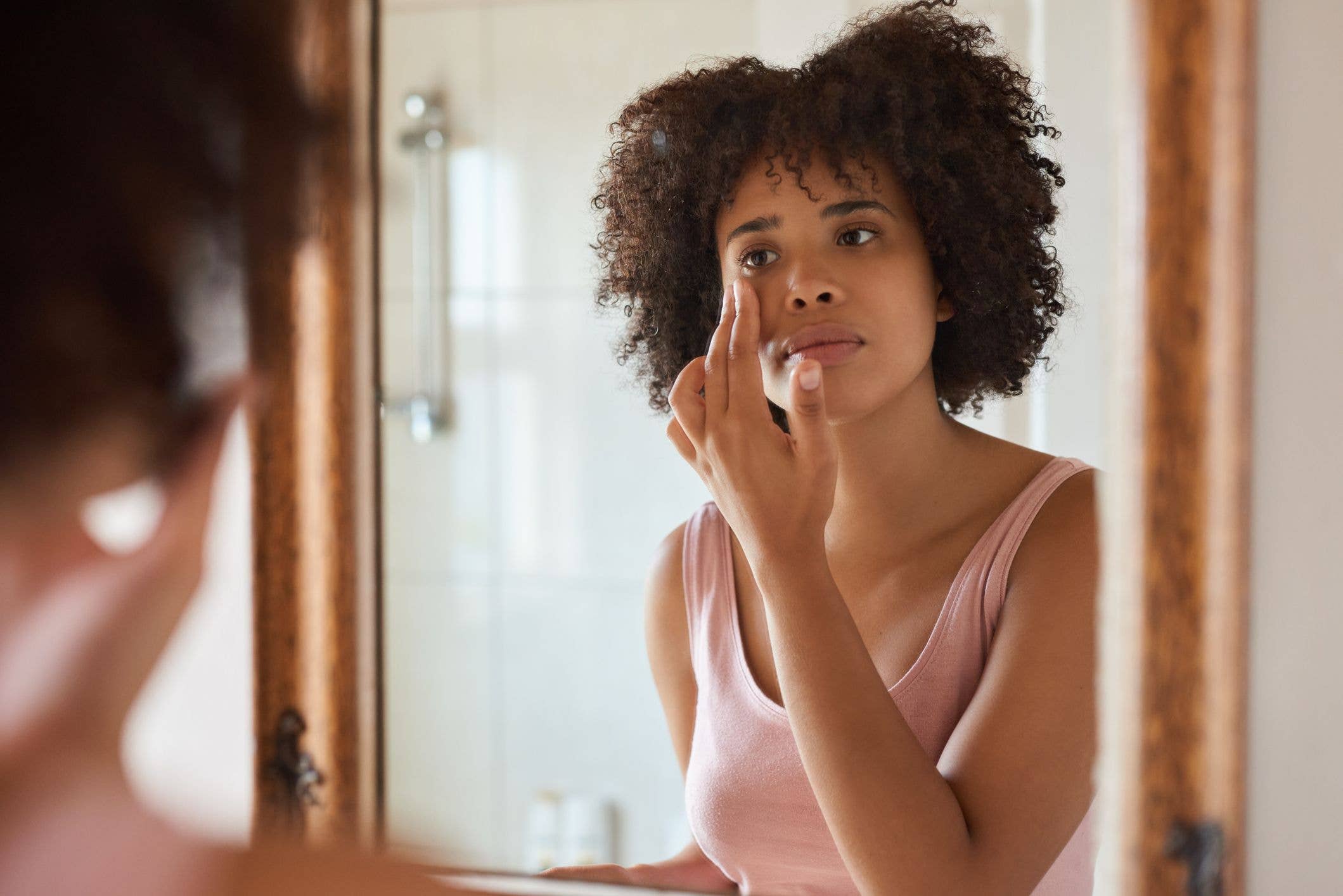  woman putting moisturizer on her face while getting ready in her bathroom in the morning