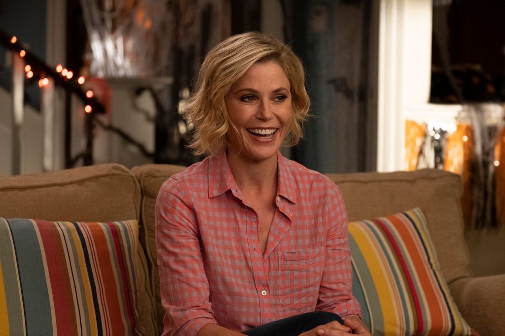 Julie Bowen smiles while sitting on a sofa as Claire Dunphy in Modern Family.