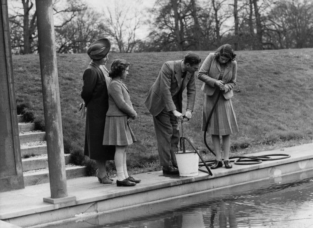 Princess Elizabeth helping her father, King George VI (1895 - 1952) with a swimming pool stirrup pump, at the Royal Lodge, Windsor, whilst Princess Margaret (1930 - 2002) and Queen Elizabeth look on