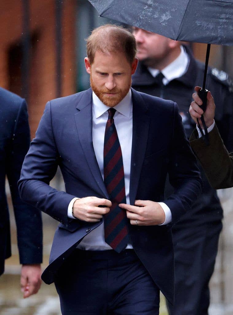 Prince Harry looking downbeat as he walks with an umbrella held over him
