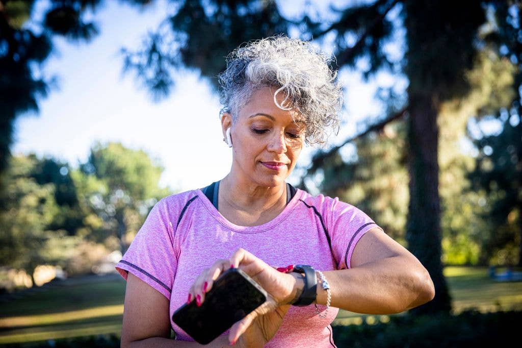Woman over 60 checking her smartwatch while walking in a park, representing the 8,000-step health target