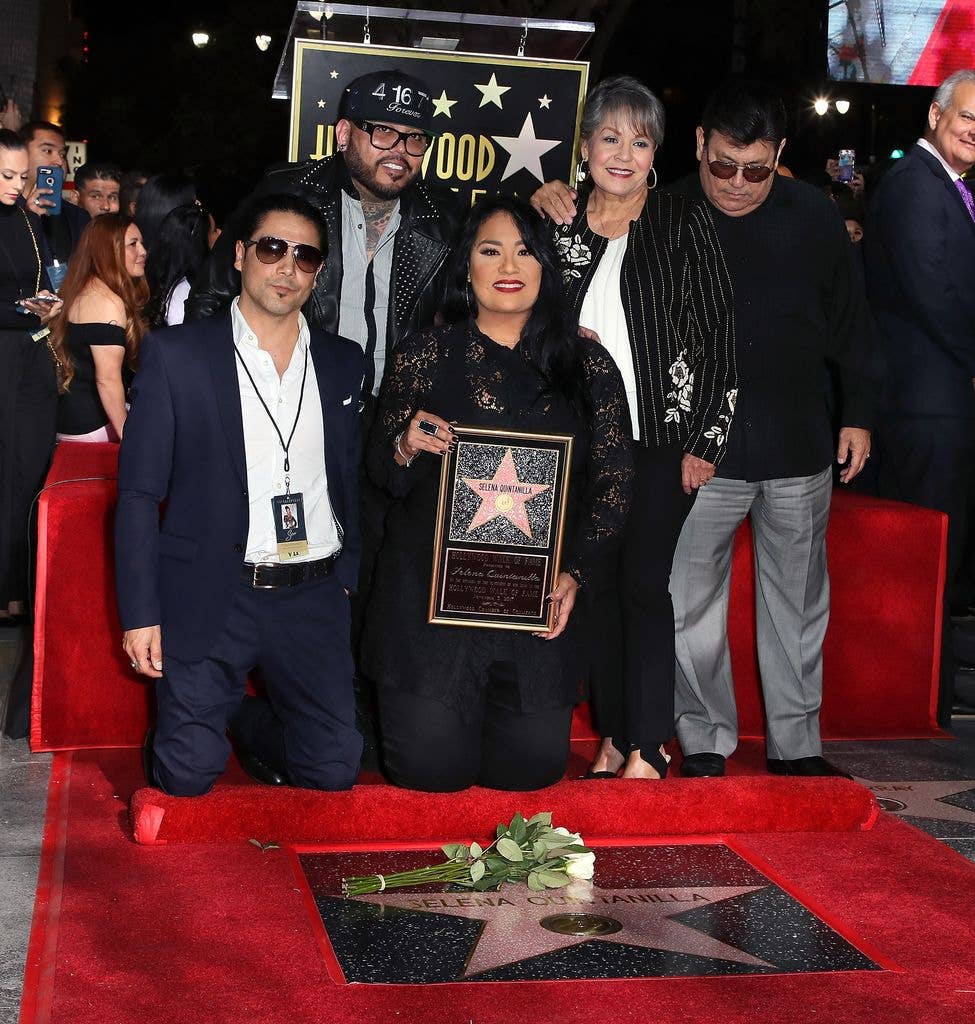 Selena's widower Chris Perez, Selena's brother A.B. Quintanilla III,, Selena's sister Suzette Quintanilla and Selena's mother and father Marcella Samora and Abraham Quintanilla Jr. kneel and stand on the red carpet around Selena Quintanilla's Hollywood Star. 