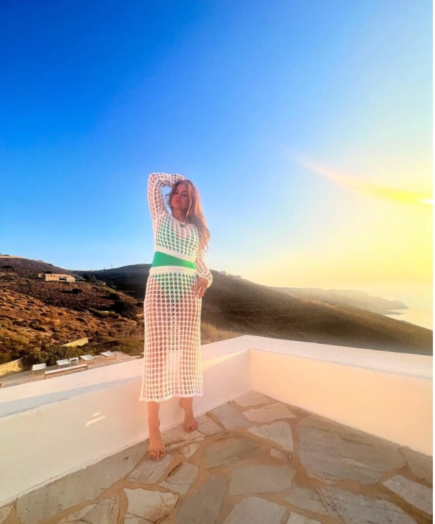 Isla Fisher posing in a green swimsuit and white cover up by the sunset