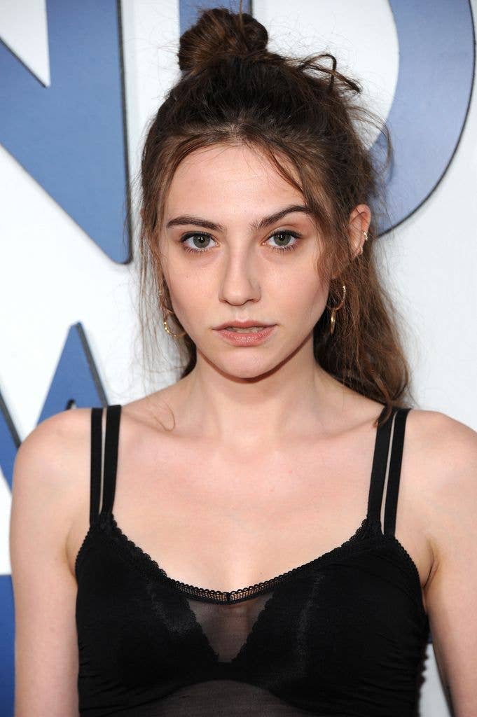 Romy Byrne in a black sheer tank top over a black bra with part of her hair up in a bun, looks directly at the camera.