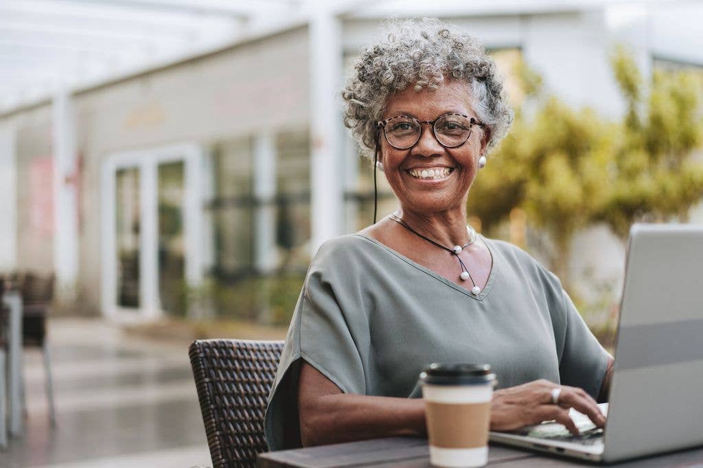 senior black woman with grey curly hair working on laptop outside in coffee shop
