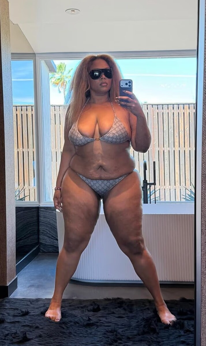 Lizzo can be seen posing in front of a floor-length mirror, standing on a plush black rug with a bathtub behind her