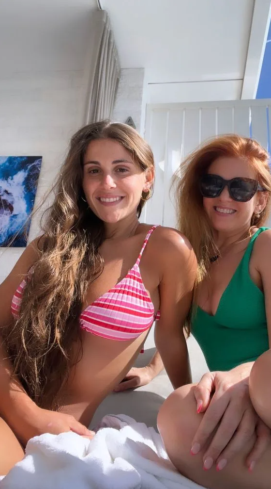 Isla smiling in a green swimsuit wearing sunglasses next to her friend in a pink patterned bikini top