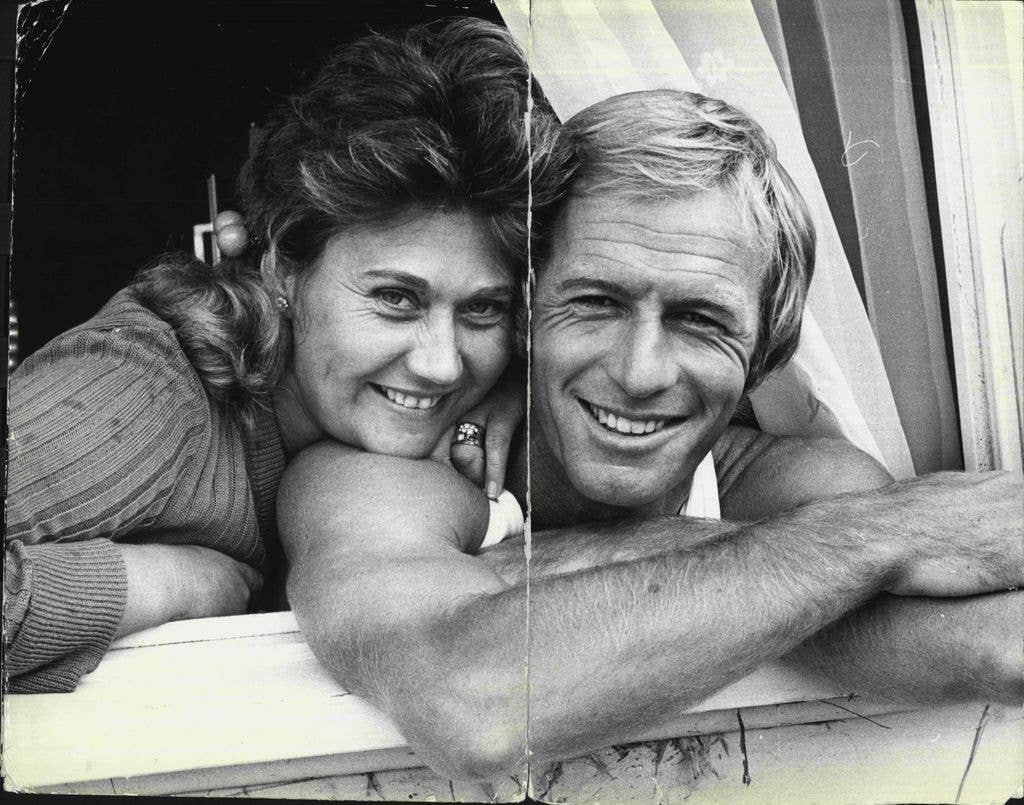 Paul Hogan and wife Noelene lean out of a window, Noelene resting her chin on her husband's shoulder.