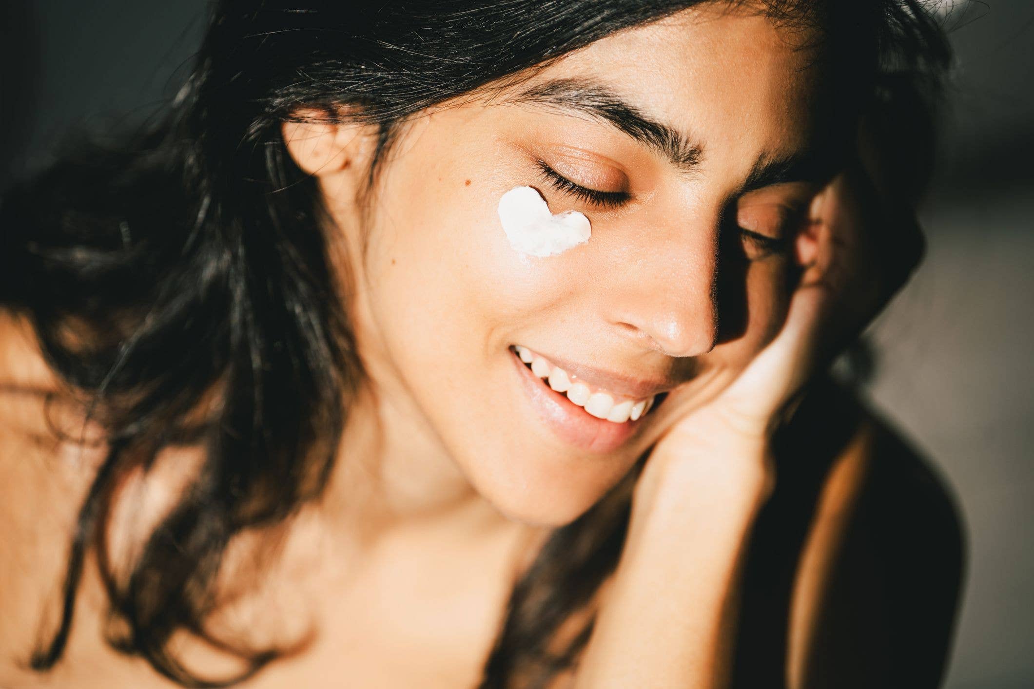 A beautiful Asian woman enjoying a morning skincare routine, applying a sunblocking moisturizer to her skin. She is smiling in the sun with her eyes closed. Concepts of no-makeup, notox, natural beauty, psychodermatology, and anti-aging SPF products to target UV damage and prevent sun damage. Versatile, functional products are the future of science-based skin care and cosmetology, products carefully selected for specific skin types with AI technology.
