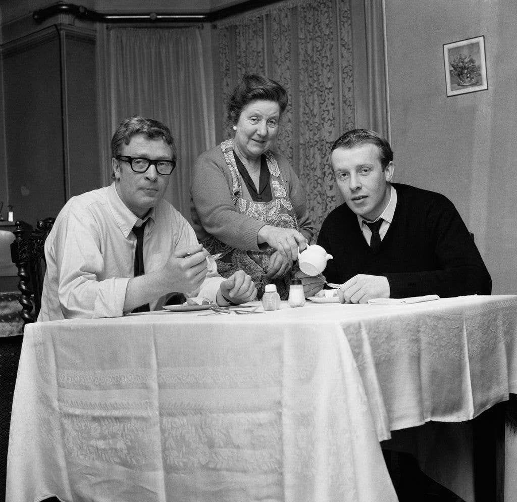Black-and-white photo of Michael Caine and Stanley Caine sitting around a table with Ellen Frances Marie pouring tea