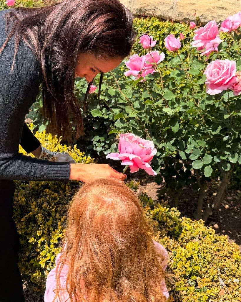 Princess Lilibet Diana looks on as her mom Meghan Markle tends to a rose in their garden
