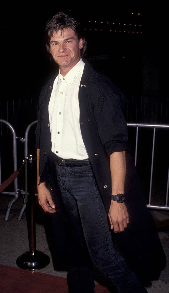 Don Swazye wears a black cardigan, white shirt and jeans and stands at an angle to the camera smiling.