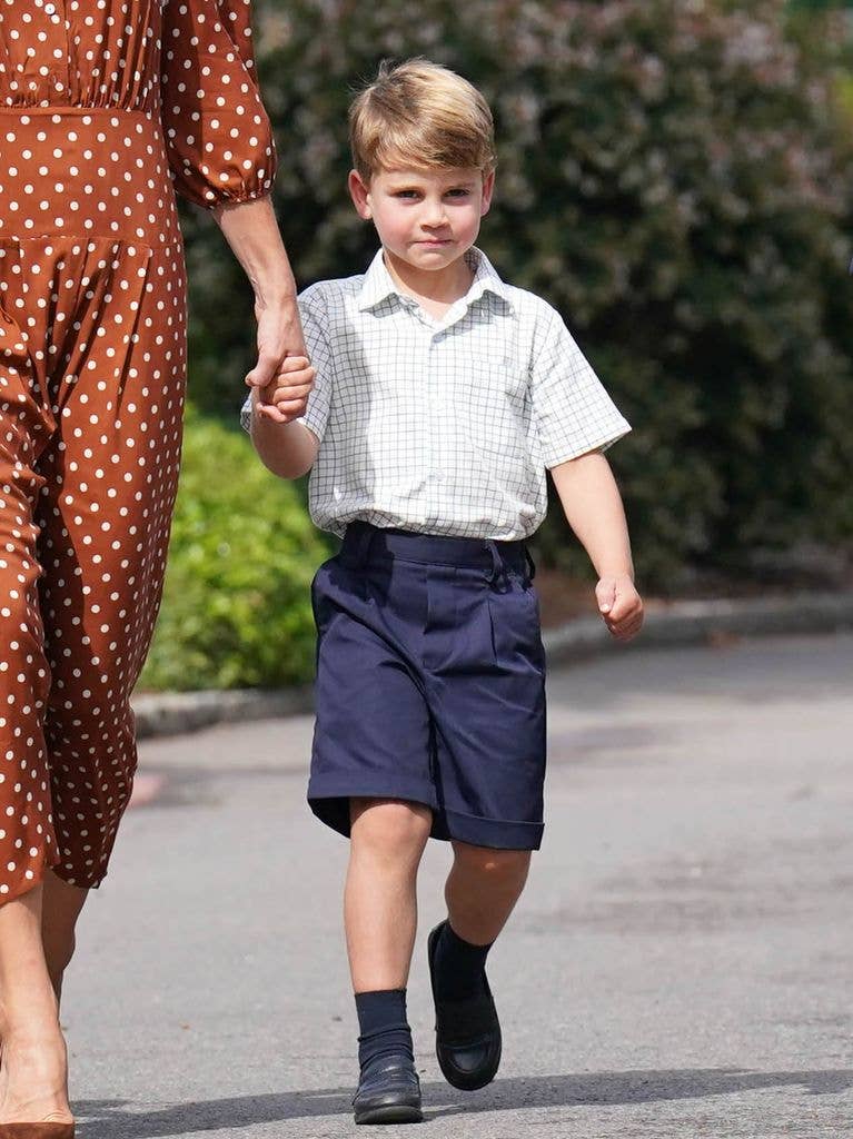 Prince Louis walks hand in hand with his mother in blue shorts and a short sleeved shirt.