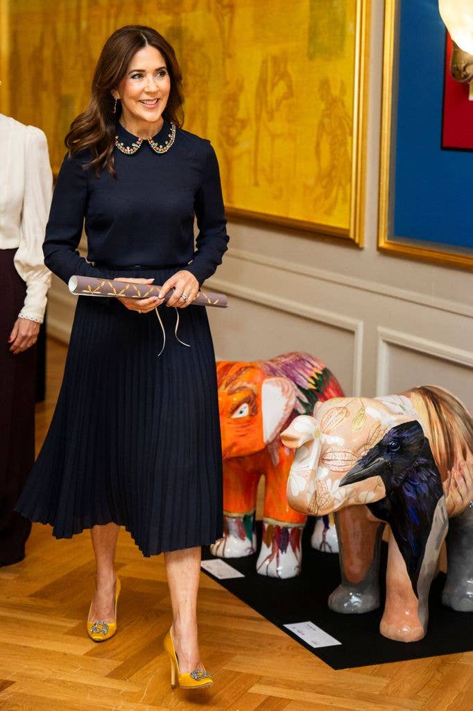 Queen Mary smiling in navy midi dress and yellow heels