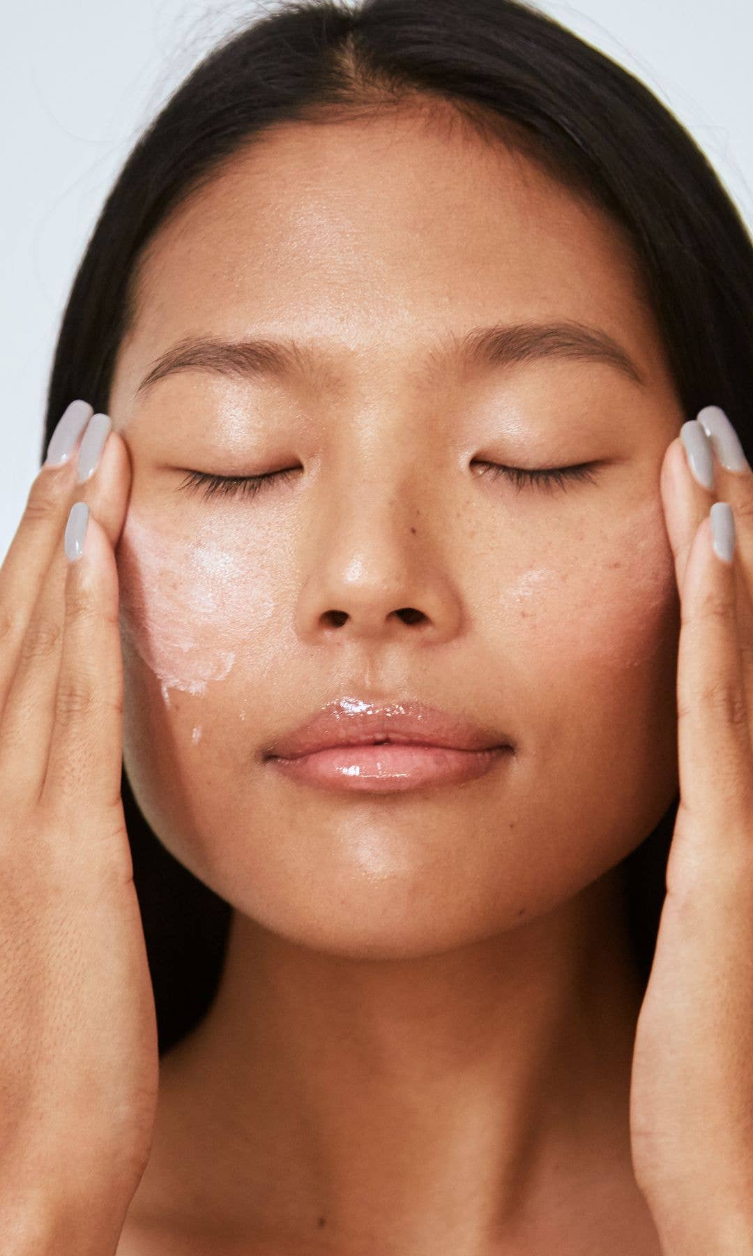 A model applying moisturiser to her skin with her eyes closed