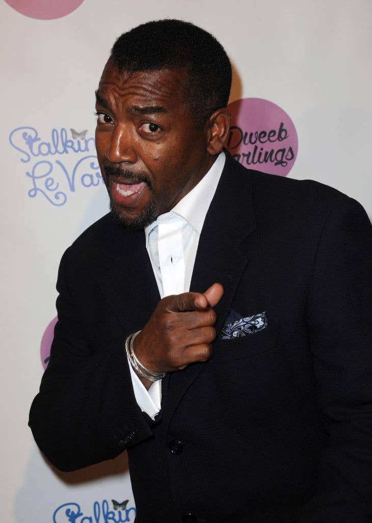 Russell in a suit, pointing finger at the camera with a smile on his face