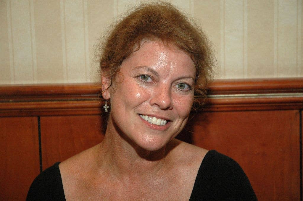 Erin Moran in a black top sitting against a half panelled wall.