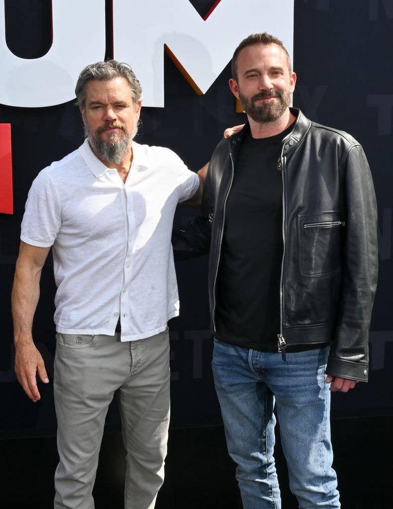 Matt Damon in a white shirt and grey trousers and Ben Affleck in a black shirt and leather jacket and jeans.