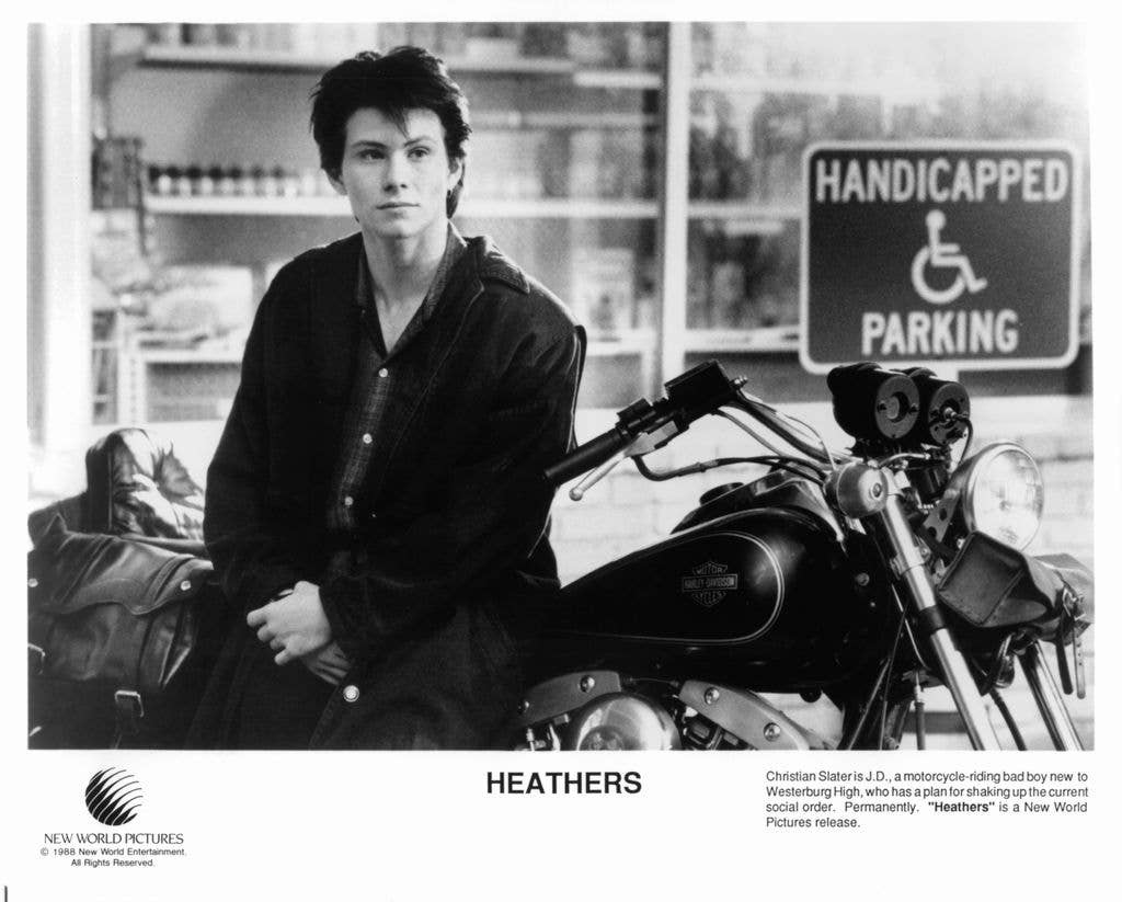 Christian Slater standing against a motorcycle in a scene from 'Heathers'.