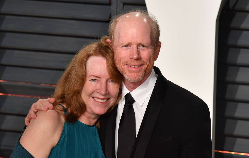Cheryl Howard wears a dark blue dress and rests her head on husband Ron Howard's shoulder. Ron wears a suit and tie, holding his right arm around his wife's shoulders.