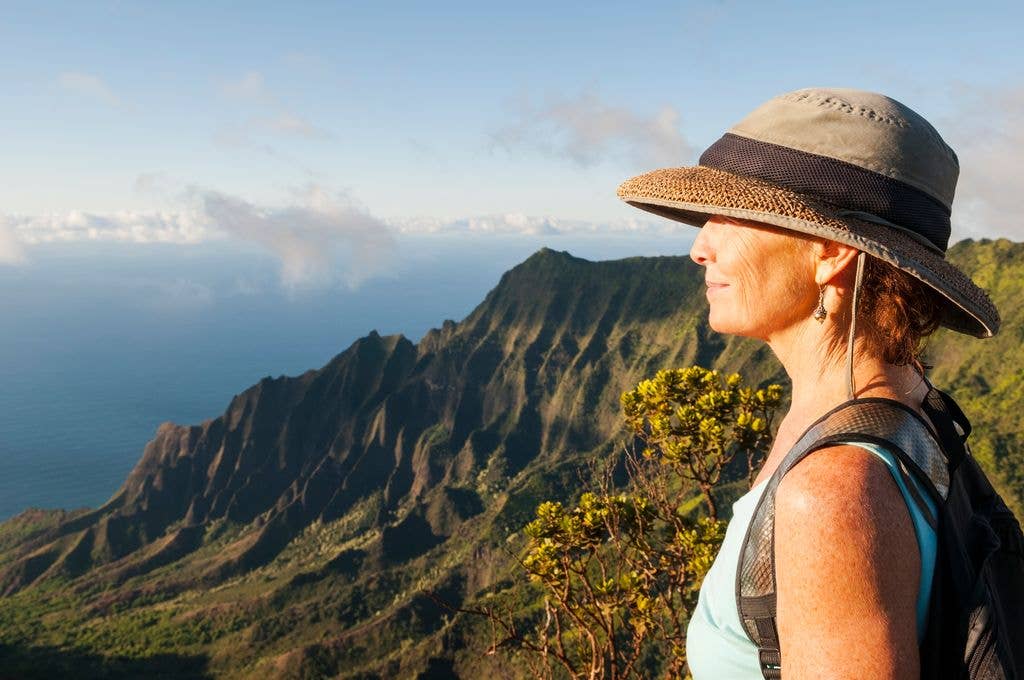 A woman looks out at the dramatic, time-worn landscape at Kalalau Lookout on Kauai, Hawaiian Islands