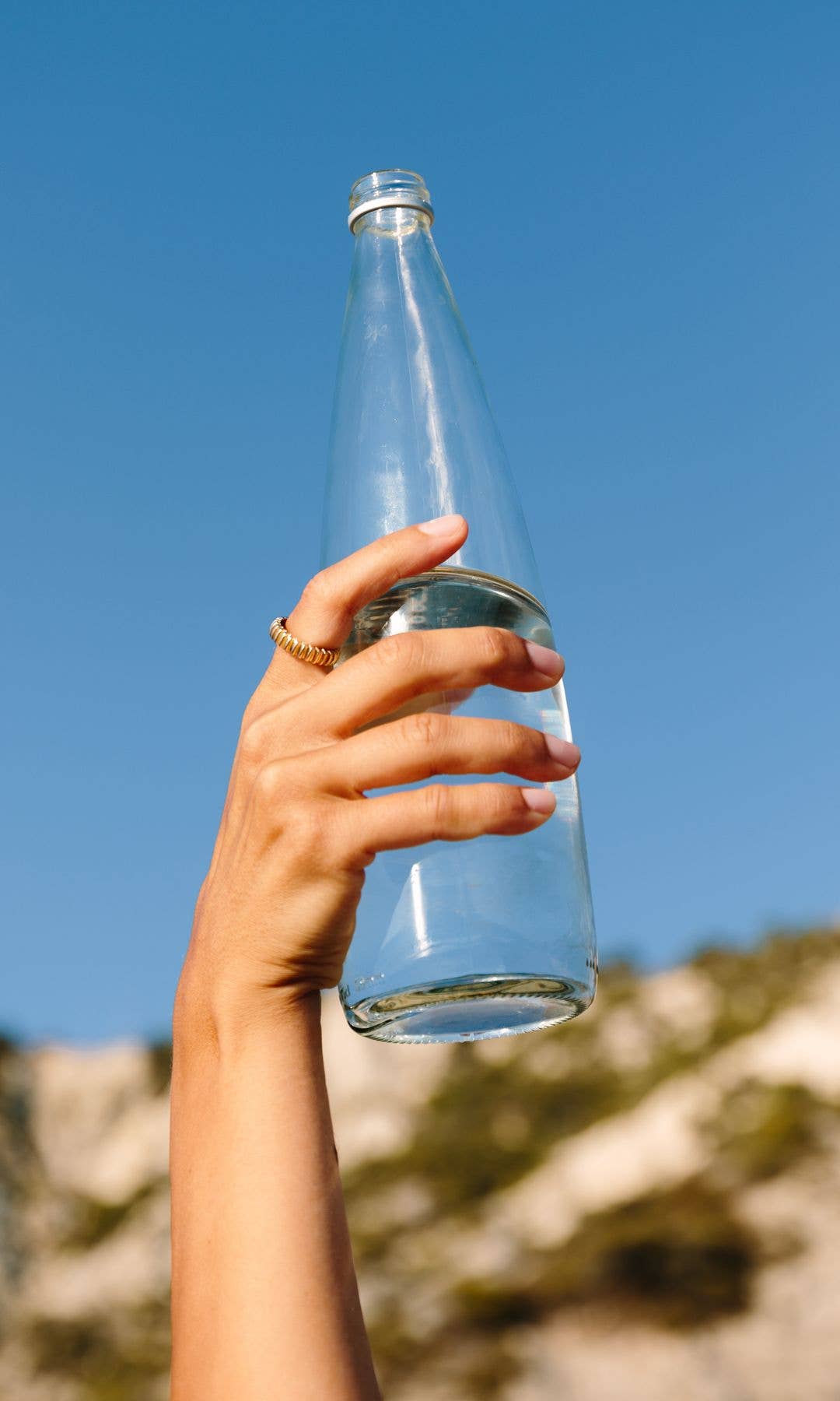 Hand holding glass waterbottle against a blue sky