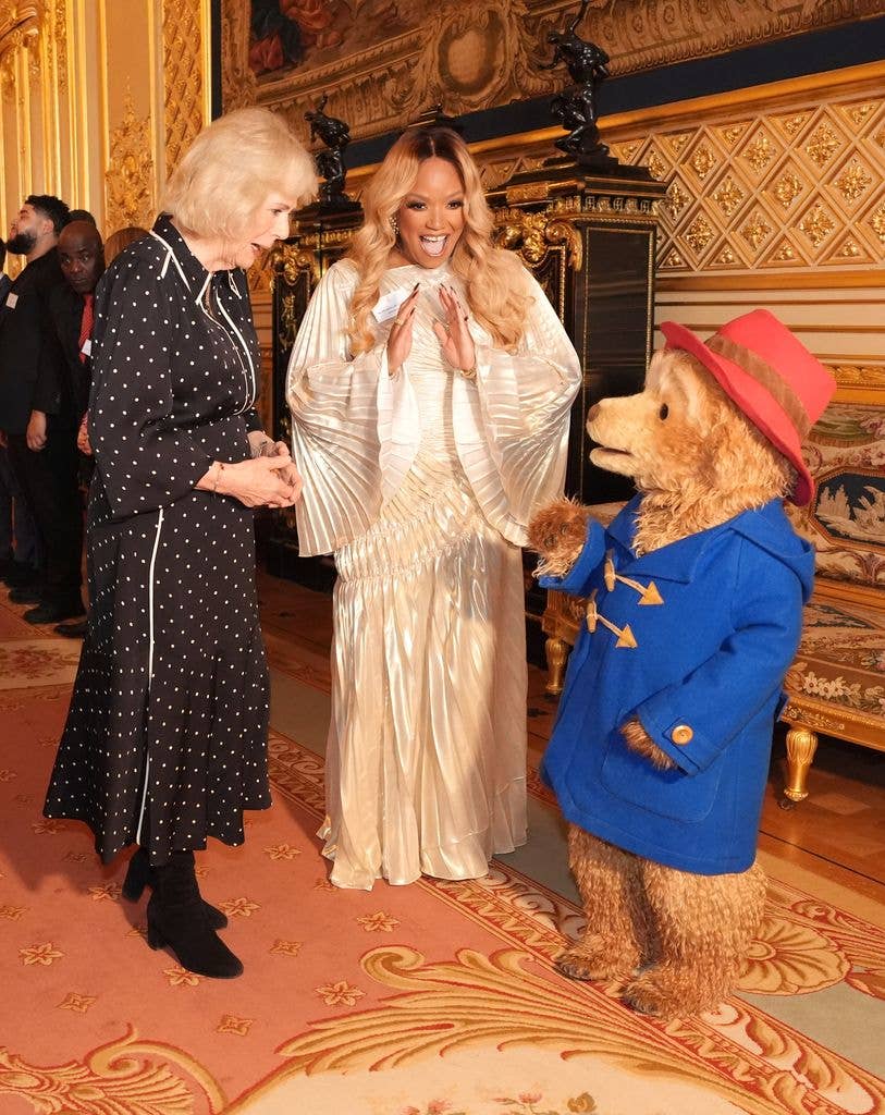 WINDSOR, ENGLAND - FEBRUARY 25: Queen Camilla greets Paddington Bear and Marisha Wallace during a reception with finalists, judges and celebrity readers, to celebrate the final of BBC's creative writing competition 500 Words at Windsor Castle on February 25, 2026 in Windsor, England. (Photo by Jonathan Brady - Pool/Getty Images)