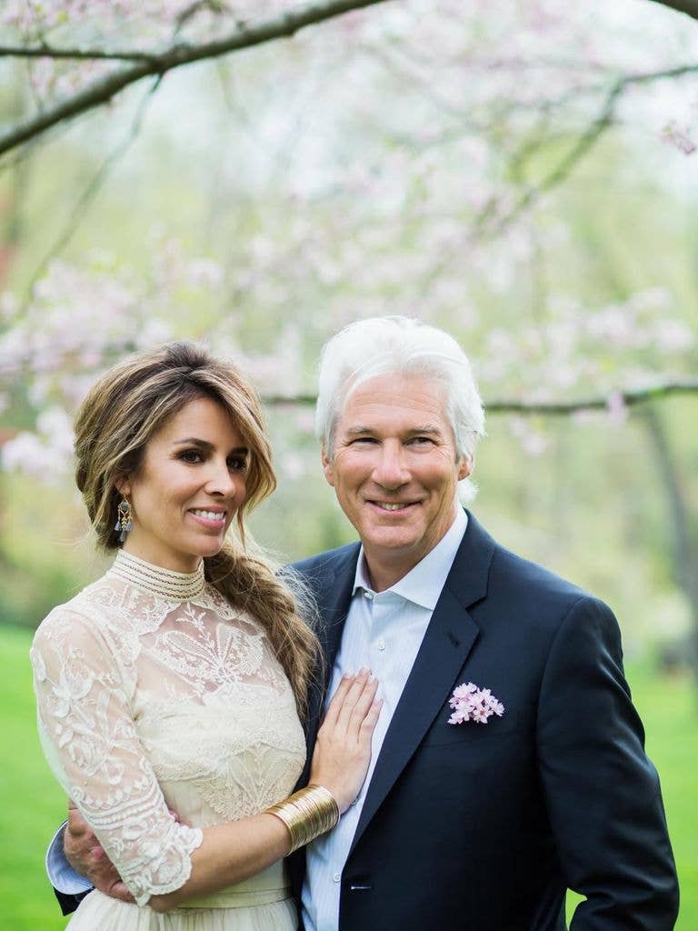 Richard Gere and Alejandra Silva smiling and posing together in a park with blooming trees.