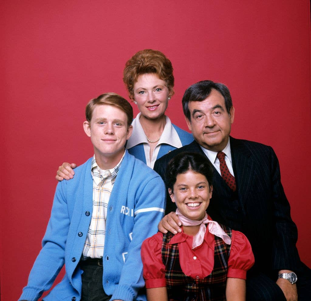 Tom Bosley, Marion Ross, Erin Moran and Ron Howard from Happy Days pose in front of a red backdrop.