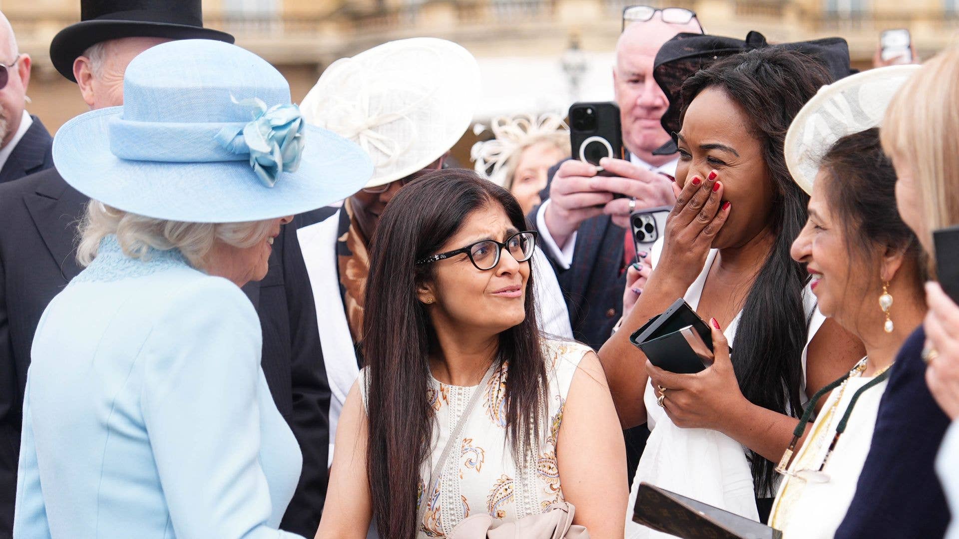 Queen Camilla laughing with guests at a Buckingham Palace garden party