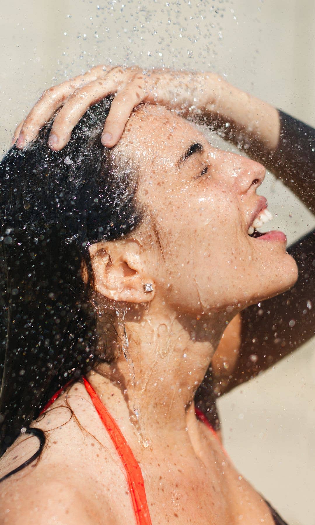 Woman in an outdoor shower with her face getting splashed by the water