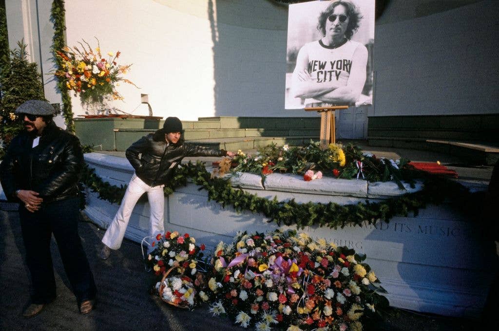 A fan places flowers below a photo of John Lennon during a vigil for John Lennon at the Naumburg Bandshell in Central Park, New York, December 14th 1980