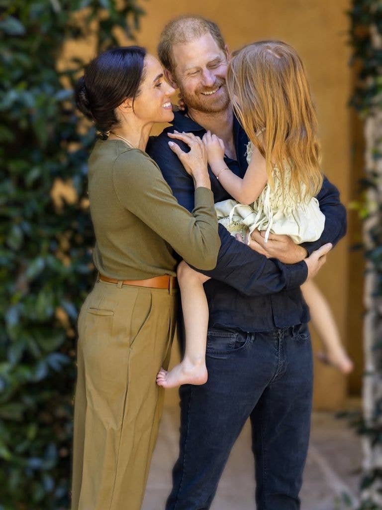 Prince Harry and Meghan, Duchess of Sussex, smiling and holding a young girl.