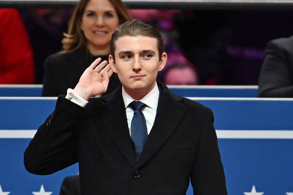 Barron Trump puts hand to ear with gesture wearing suit