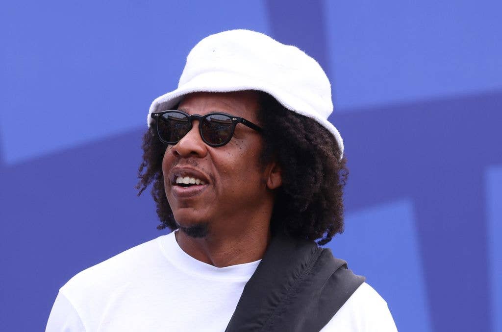 Jay-Z smiles wearing a white hat and sunglasses