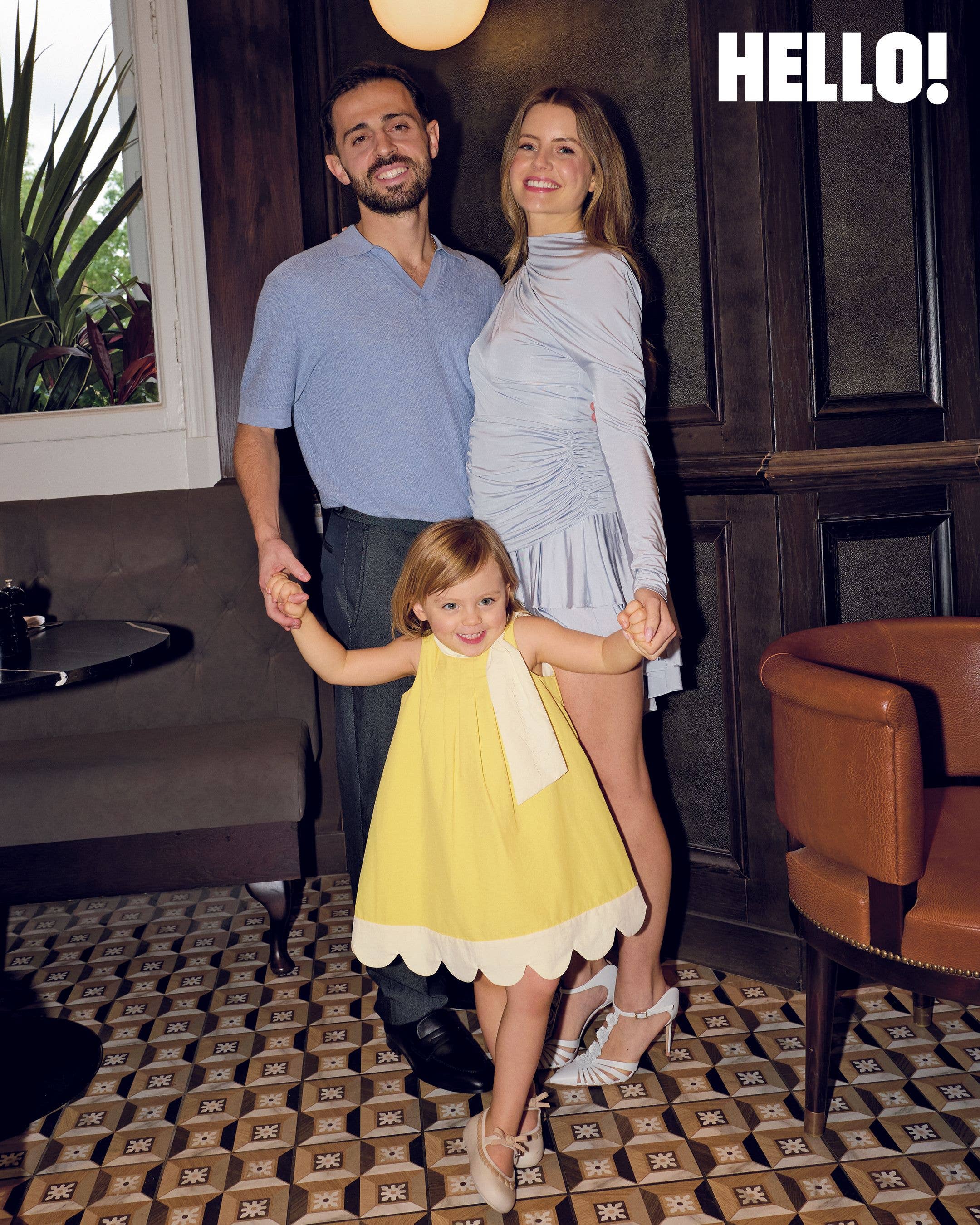 Bernardo and Inês Silva each hold one of their daughter Carlota's hands as she wears a yellow dress with a scalloped hem